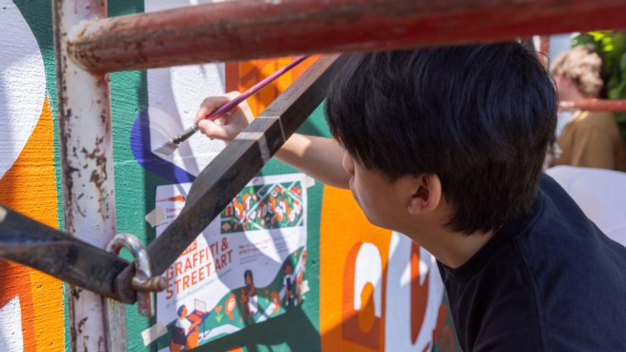 A student is up close with the mural, painting a detailed area of the wall. 