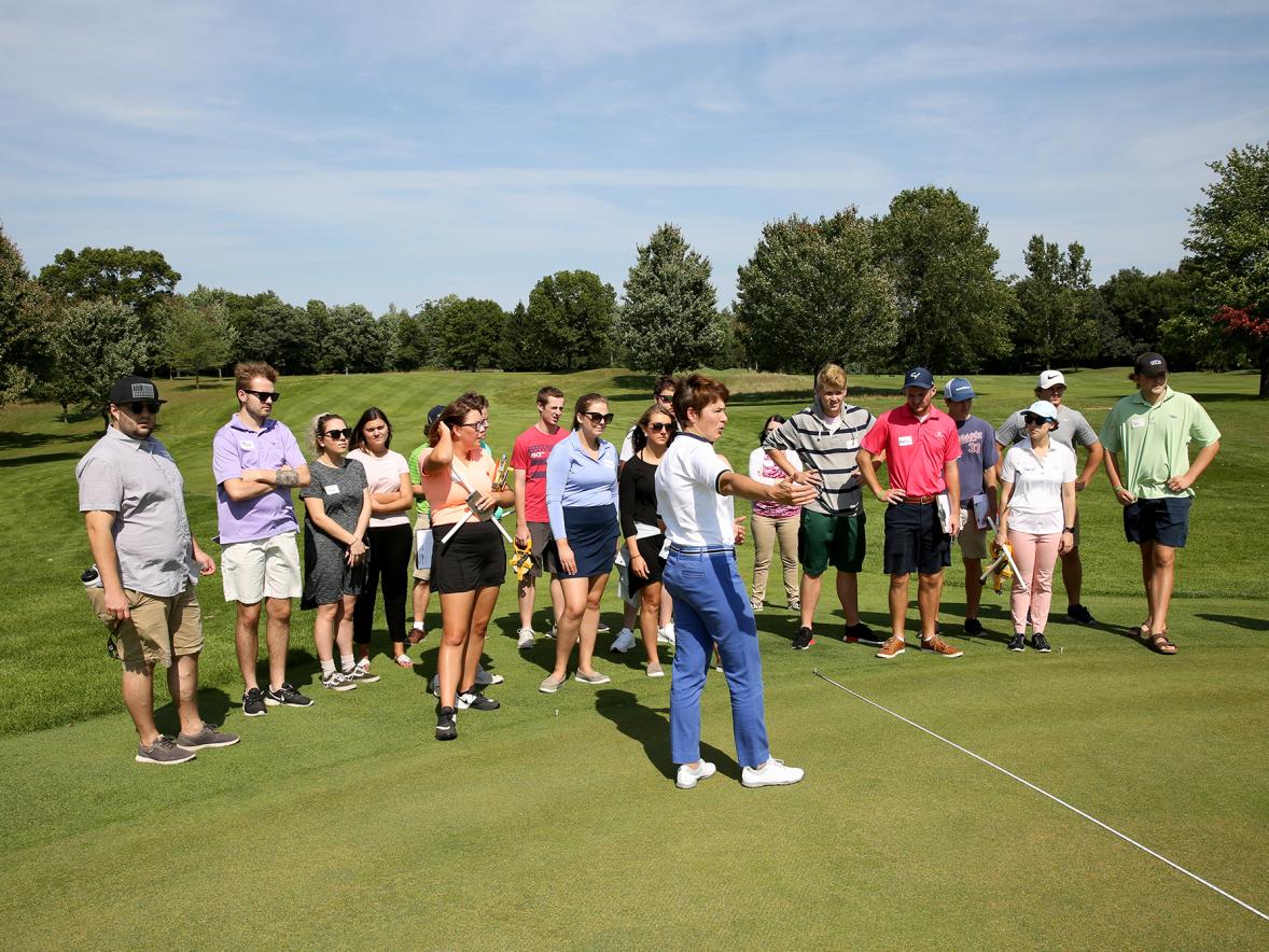 A Sports Event Management class listens to Associate Professor Kris Schoonover at Tanglewood Greens, where the Tees Fore Tuition event will be held.