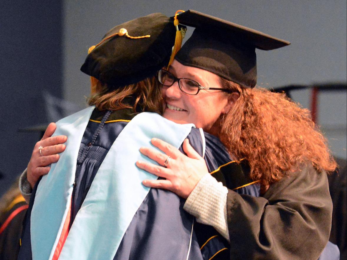 Dione Schumann hugs her program adviser while crossing the commencement stage Dec. 14.
