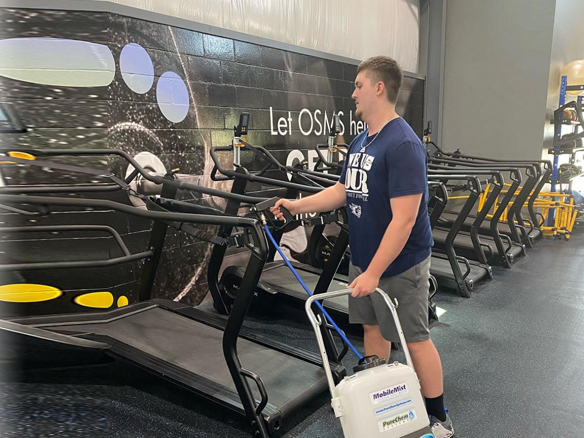 UW-Stout student Matt Rotter disinfects gym equipment at Synergy Sports Performance in Hobart using a MobileMist. Over the summer Rotter did a Cooperative Education and Internship Program at a Green Bay company that has products designed to curb the spread of COVID-19.