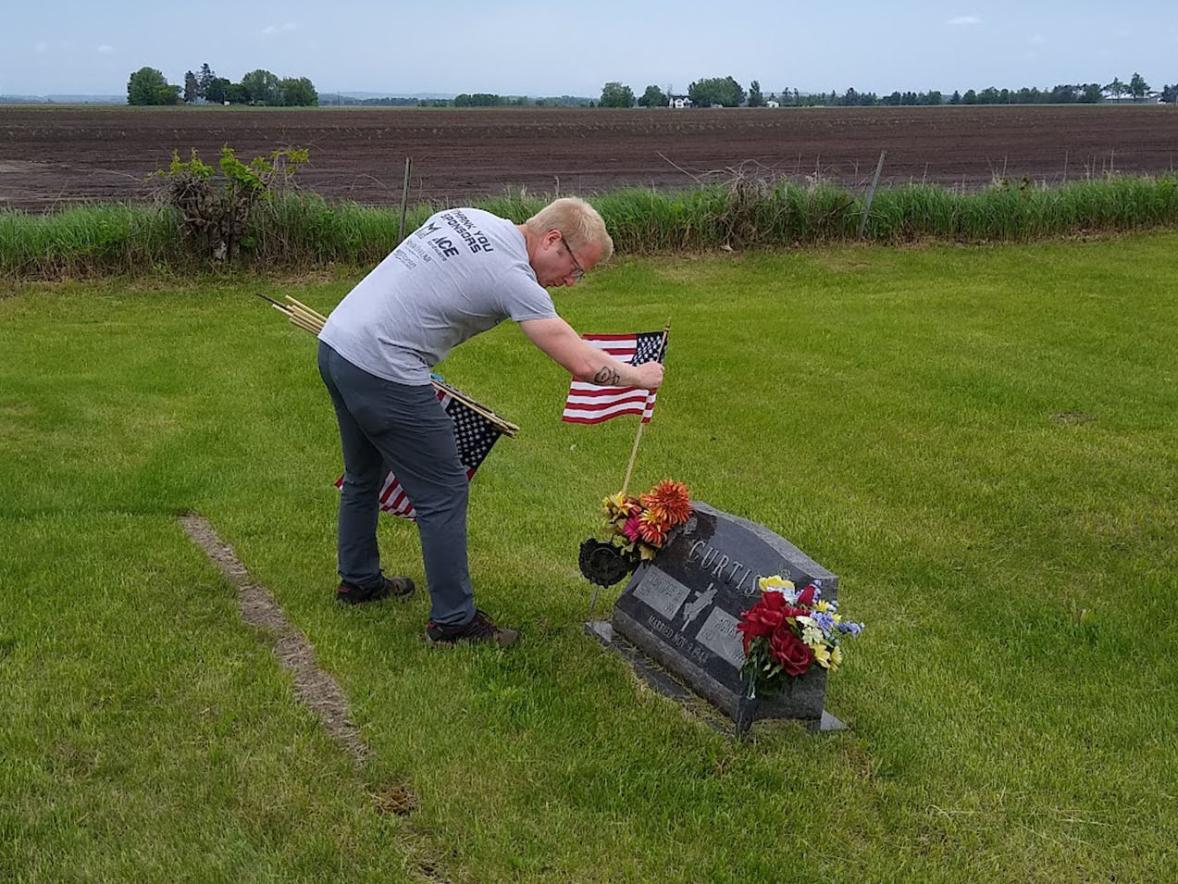 Veterans Club President Eric Gritzmacher places a U.S. flag at the gravesite of a veteran at Falls City Cemetery.